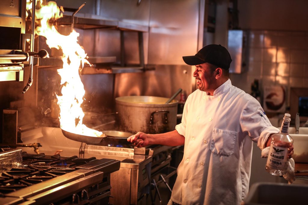 Fire shooting up from a frying pan as a chef cooks food over a propane stove