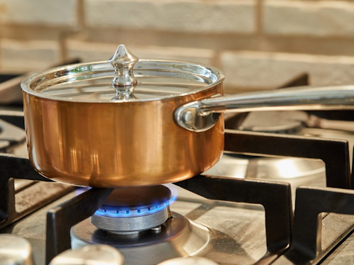 A copper saucepan heating on low on a gas stovetop